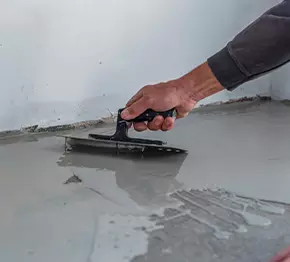 Ruka pracovníka uhladzuje čerstvo nanesený betón pomocou hladidla počas stavebných prác.